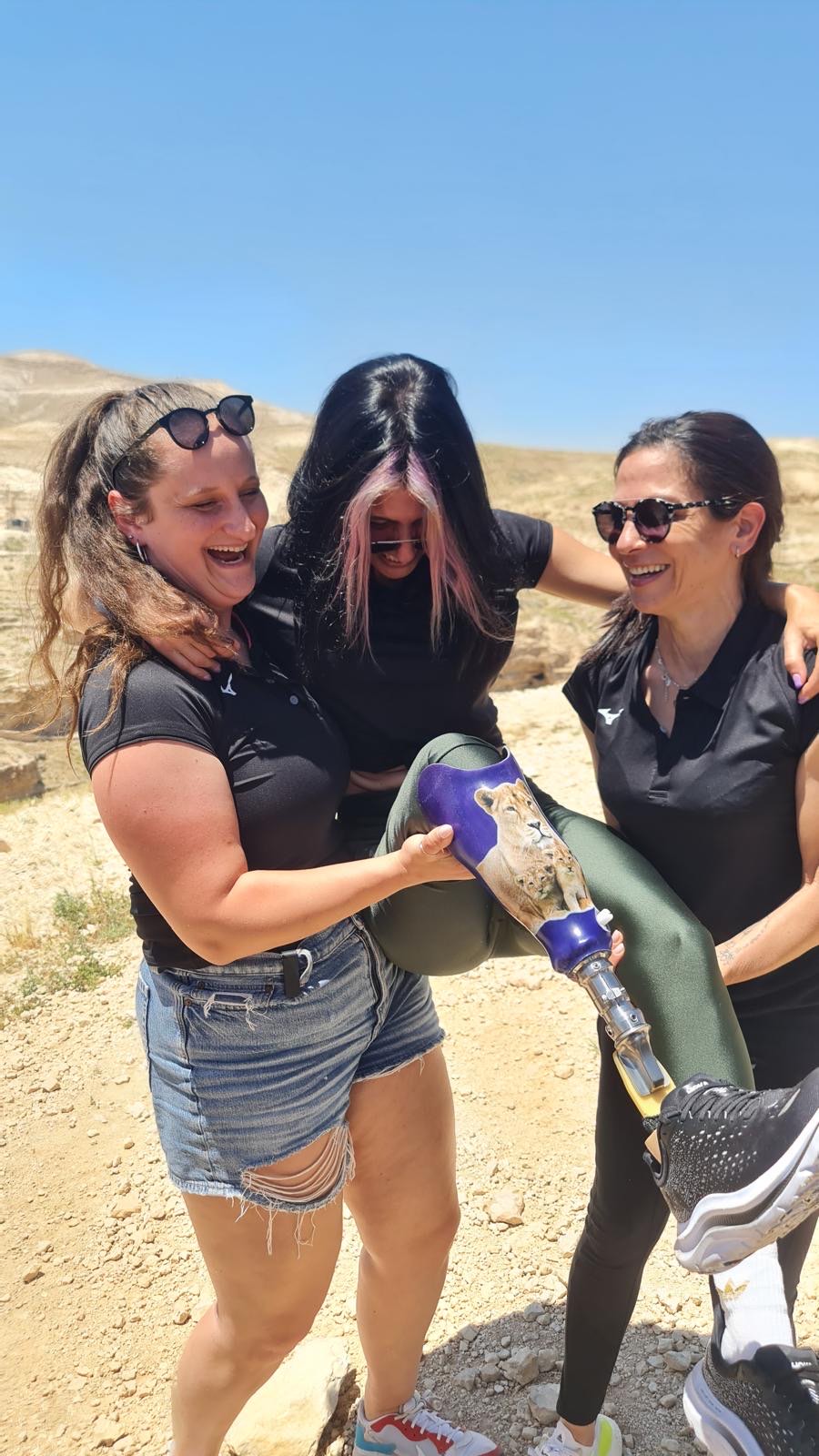 שלוש נשים צוחקות ונושאות יחד חברה עם רגל תותבת בטיול במדבר