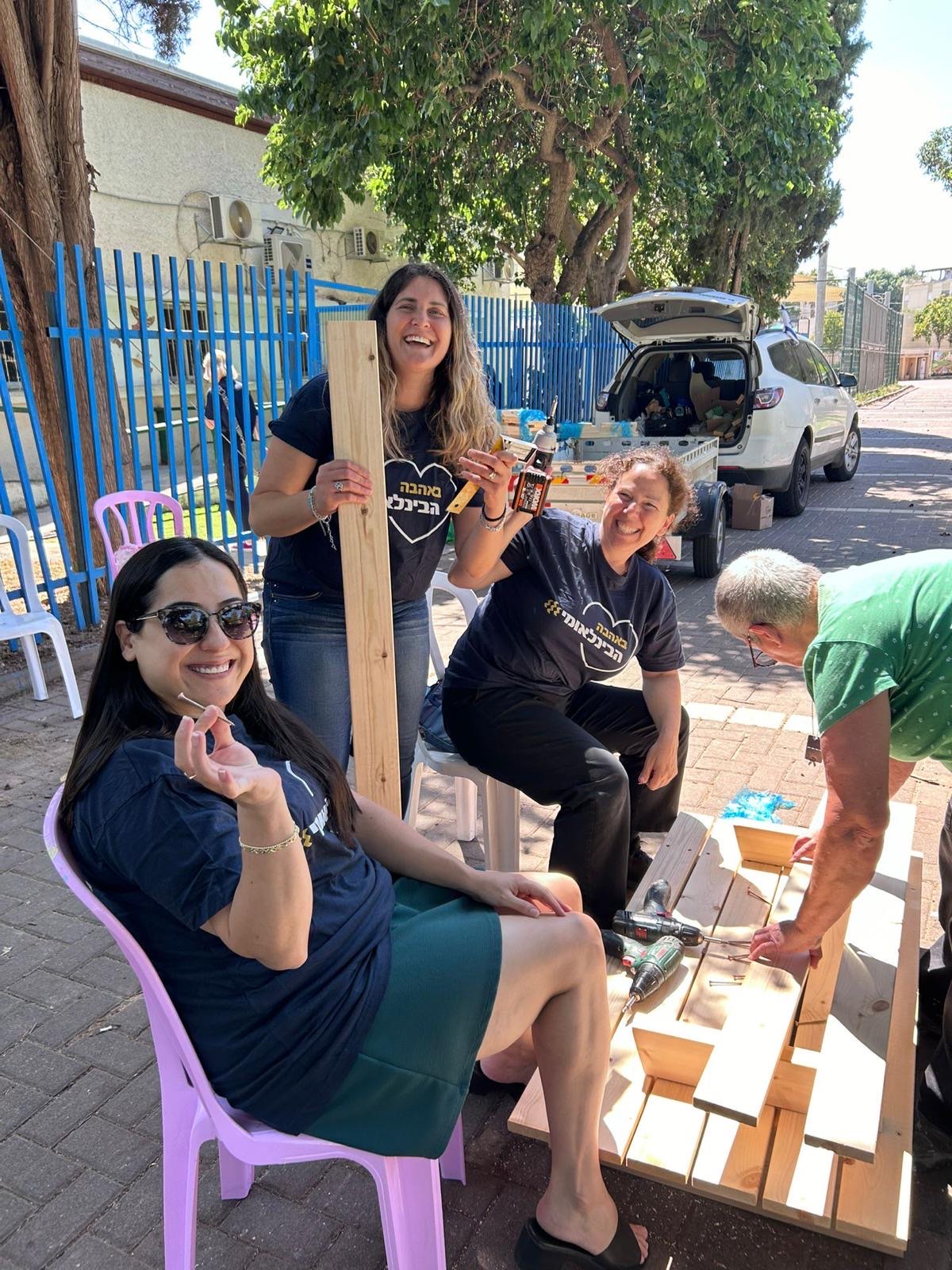נשים מחייכות בונות יחד ריהוט עץ בהתנדבות ביום המעשים הטובים
