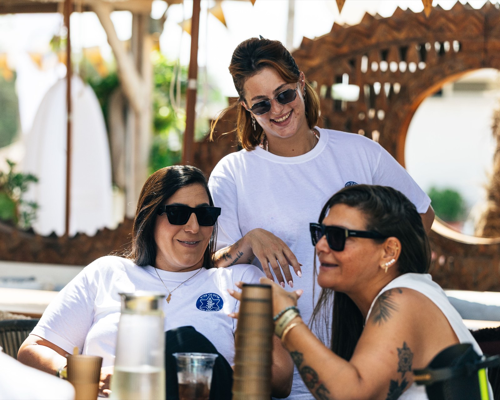 שלוש נשים בחולצות ארגון נכי צה״ל צוחקות יחד במפגש על החוף